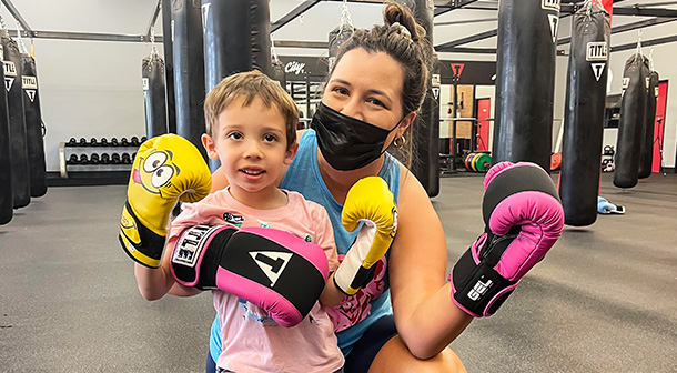 Nicole y su hijo pequeño muestran sus guantes de boxeo en un gimnasio local.
