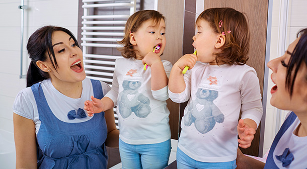A mom teachers her toddler healthy family habits by showing her how to brush her teeth.