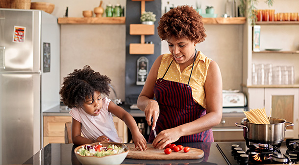 Una mamá le muestra a su hija pequeña cómo preparar una ensalada saludable en la cocina.